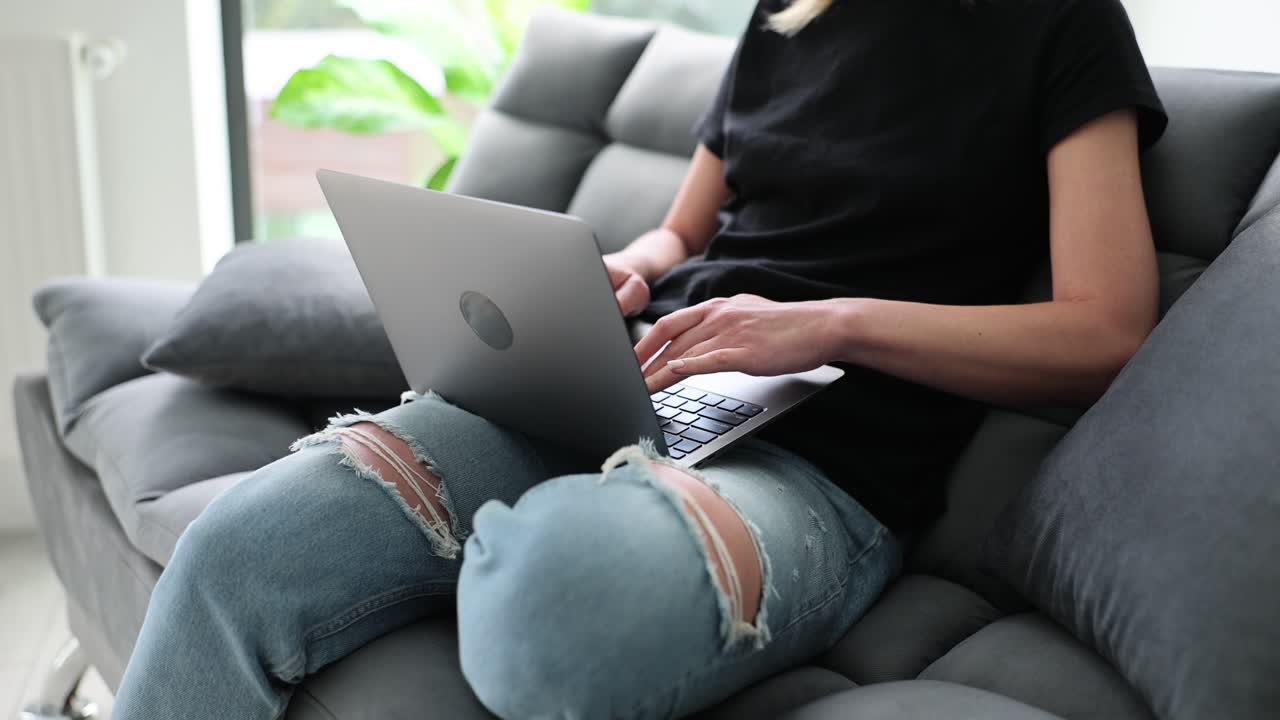 Kvinde sidder på sofaen og betjener bærbar computer i stuen