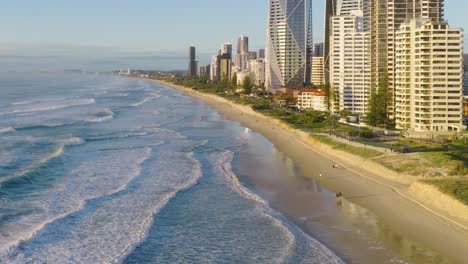 aerial footage captures gold coast's beachfront skyline with high-rise buildings, ocean waves, and sandy shores under clear skies