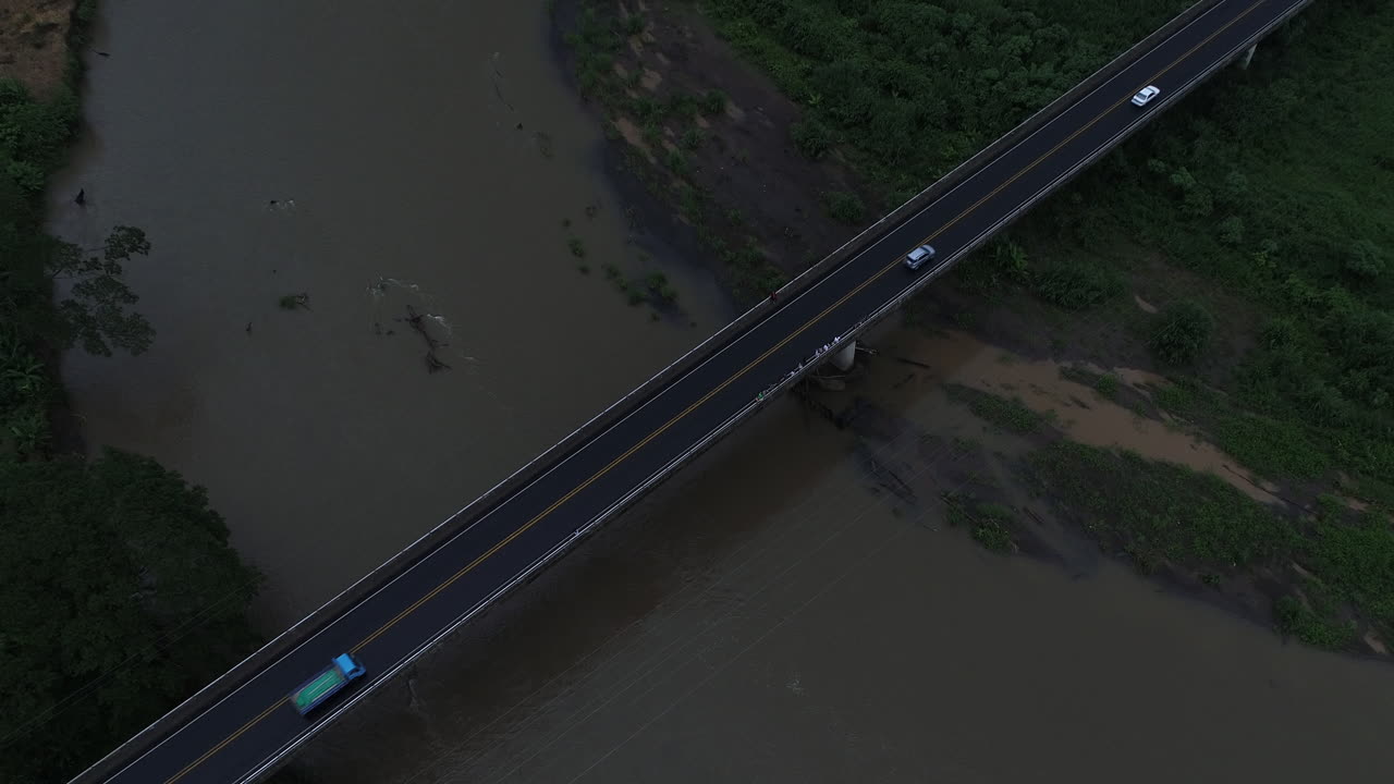 Descending aerial as cars move across Costa Rica crocodile bridge over river, 4K