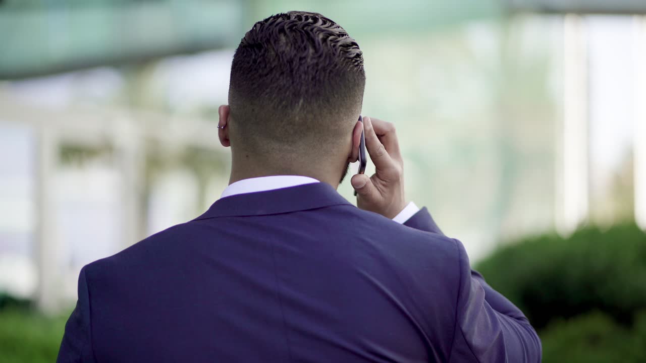 Vista de costas de empresário falando ao celular ao ar livre
