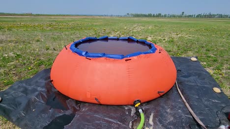 un tanque de agua naranja en la propiedad del aeropuerto, conectado a una bomba, en medio de un campo de hierba bajo un cielo despejado