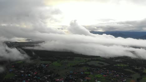 Drone-fly-over-the-remote-countryside-hills-of-Pai,-Thailand-covered-in-rolling-hills-of-green-fields-and-very-low-thick-inversion-cloud-during-monsoon-season