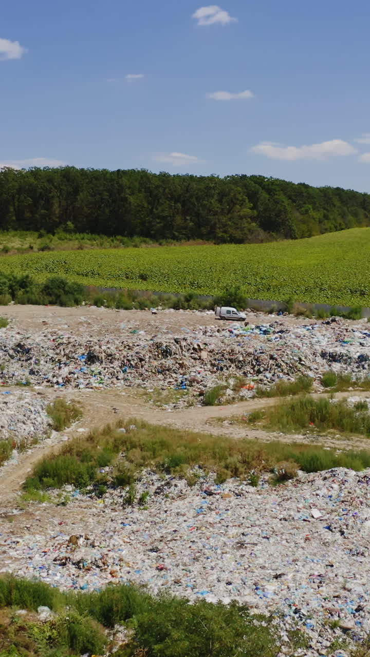 Garbage among nature. Piles of rubbish on field surrounded by green trees. Pollution of environment. Dirty litter in summer. Aerial view. Vertical video