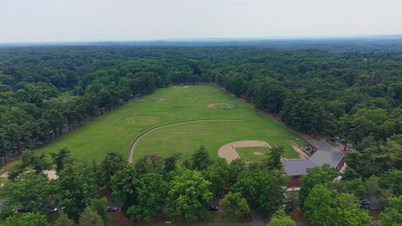 Ripresa aerea frontale con drone di un ampio complesso sportivo verde per baseball e attività ricreative, situato in una radura in mezzo a una fitta foresta, Springfield, Massachusetts, USA.