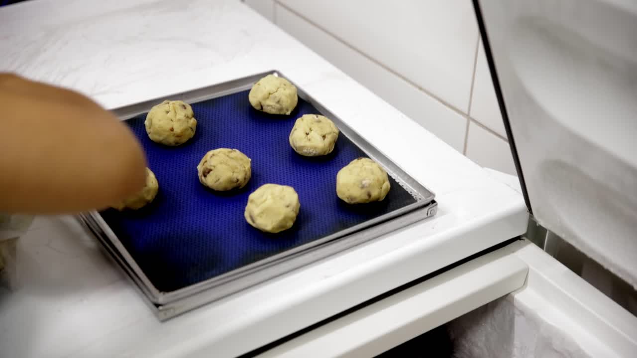 Palline congelate di impasto per biscotti con gocce di cioccolato poste su una teglia da forno per essere cotte e vendute