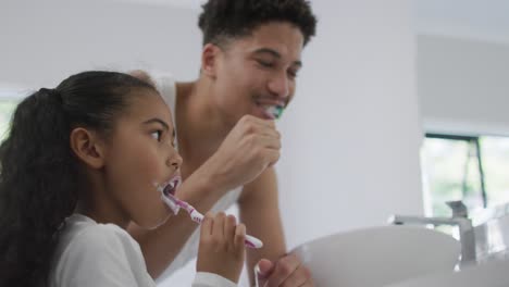 happy biracial father and daughter washing teeth in bathroom together