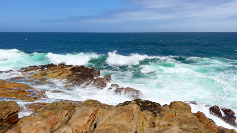 Wellen-Krachen-An-Der-Küste,-Felsbrocken,-Leuchtturm-Von-Cape-St.-Francis,-Südafrika,-Atemberaubend-Schöner-Sommertag,-Strandlandschaft,-Jbay,-Austerngartenroute,-Küstenlinie,-Zeitlupe,-Schwenk-Nach-Links