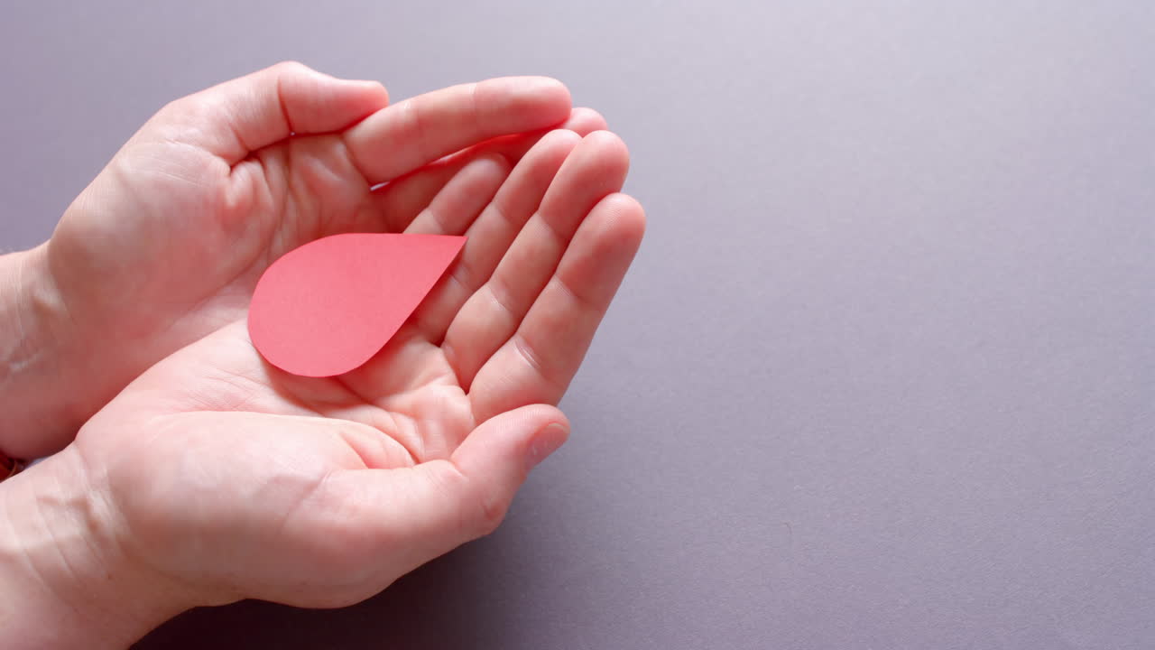 Hands of caucasian woman holding blood drop on grey background with copy space, slow motion