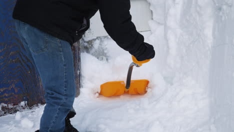 close up of man shoveling snow in front of a barn