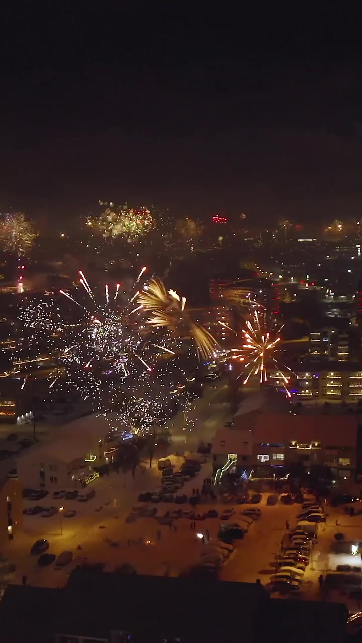 Veduta aerea con drone di vivaci fuochi d'artificio che esplodono su una città innevata di notte, celebrando il Capodanno con strade illuminate e luci festive.