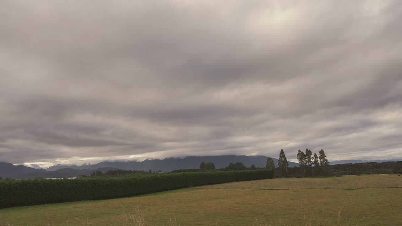 Timelapse image of a moody overcast sky rolling above rural farmlands and distant mountain ridges in New Zealand