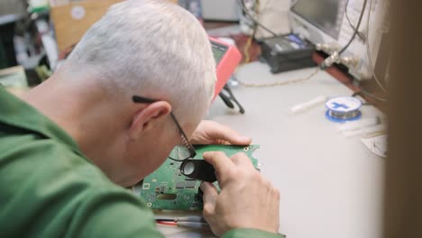 electronic equipment repair shop. the engineer technician solders the printed circuit board of an electronic device under a microscope.