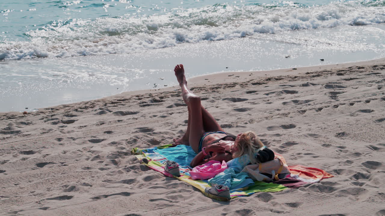 A woman in a bikini relaxes on a colorful towel by the sea, sunbathing under bright daylight