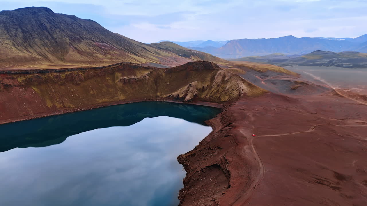 Red car stands at the sleeping volcano crater filled with water. Cosmic rocky landscapes of Iceland from top.