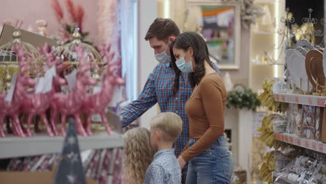 una familia con máscaras médicas en la tienda compra adornos navideños y regalos en cámara lenta.