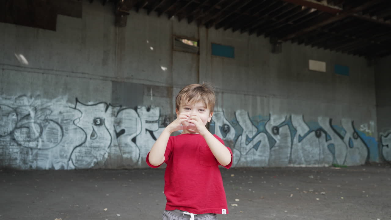 Vídeo em câmera lenta, um menino pequeno se divertindo e fazendo símbolos de coração com as mãos em frente à câmera, vestindo uma camiseta vermelha