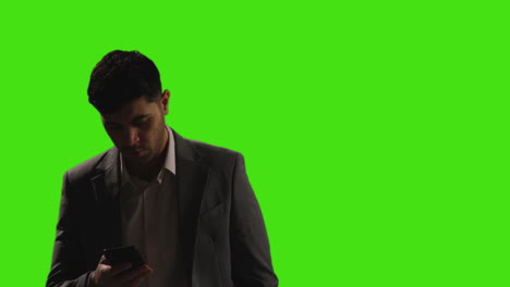businessman talking on mobile phone walking into frame against green screen background with low key lighting