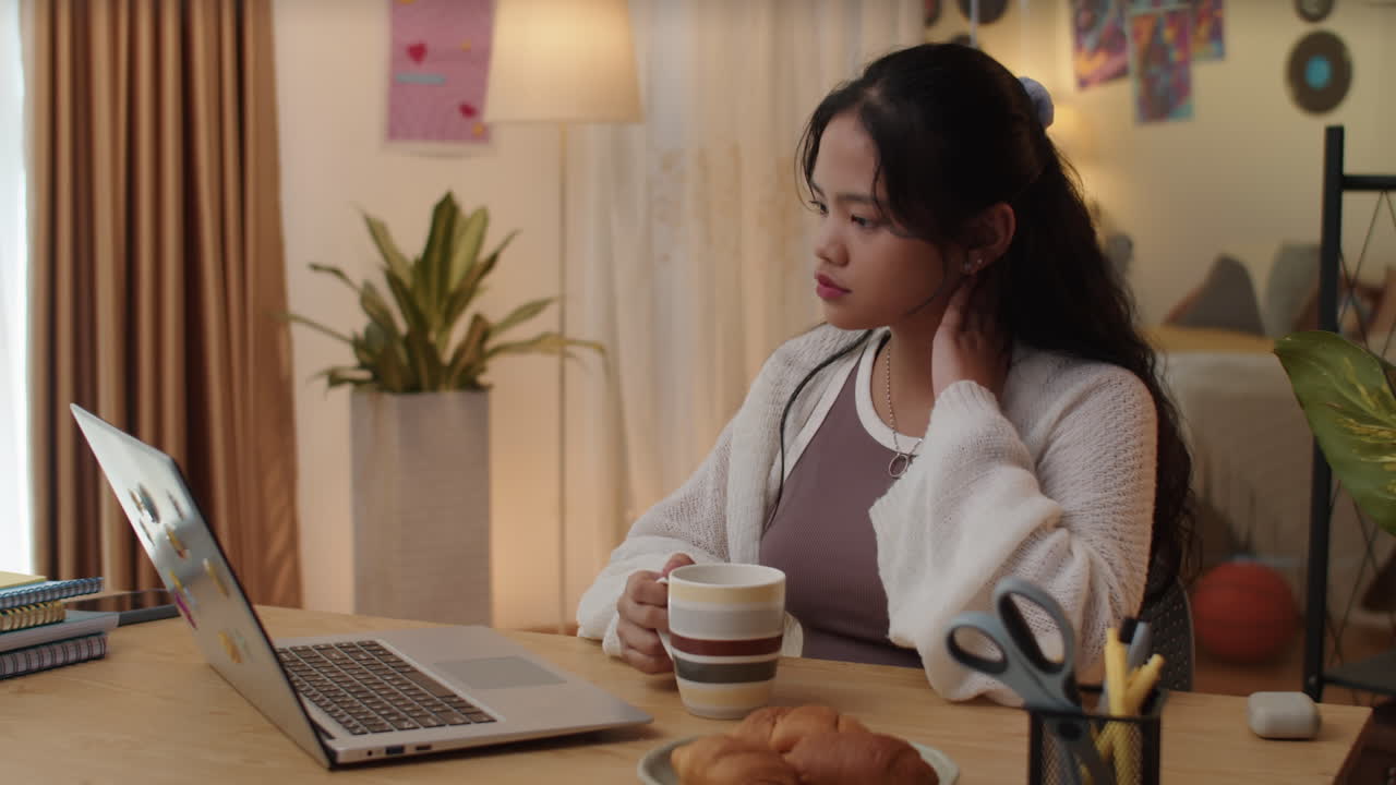 Female Student Drinking Coffee when Watching Educational Video on Laptop