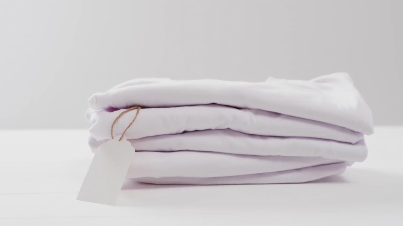 Video of stack of folded white t shirts with copy space on white background
