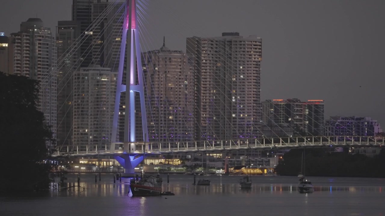 Una vista notturna mostra grattacieli residenziali accanto al Ponte Kangaroo Point illuminato di viola lungo il fiume Brisbane
