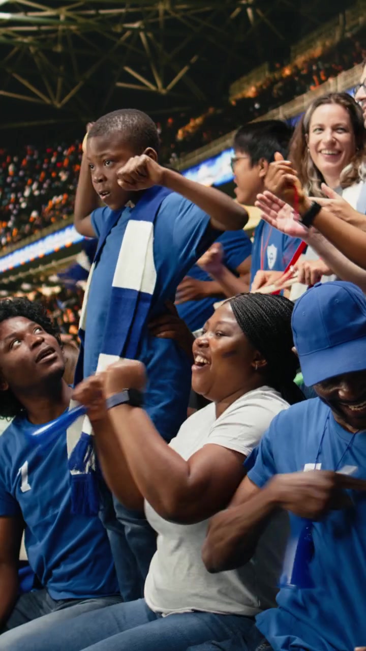 Video vertical: Joven aficionado infantil rodeado de seguidores del equipo azul animando durante un partido de fútbol