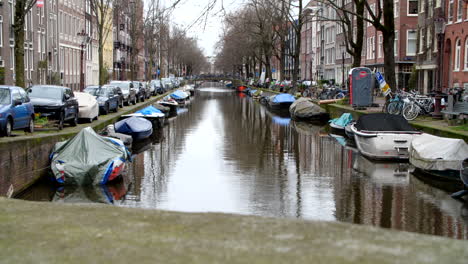 bridge view of amsterdam canal with boats, cars and water during a gloomy winter day