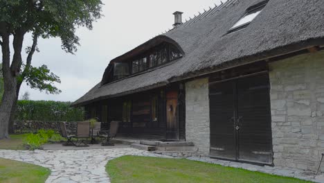 old restored limestone traditional building in saaremaa estonia that has a straw or rye roofing surrounded by limestone roads and a beautiful garden with short green mowed lawn and grass. cloudy day.