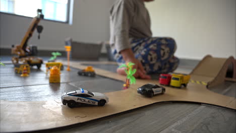 slow motion selective focus shot of a small boy playing with his car toys and his mother on a homemade cardboard track in his room