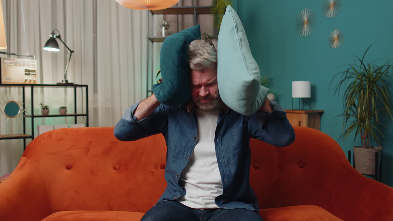 ремонтные работы у соседей концепция, раздраженный мужчина дома покрывает уши подушками раздраженный шумом