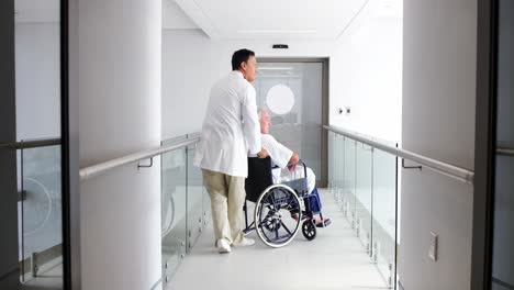 Doctor-holding-senior-patient-on-wheelchair-in-passageway