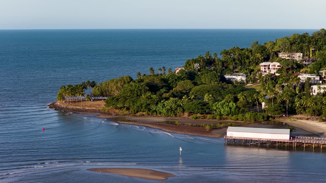 Drone captures lush tropical island with pier, surrounded by calm blue waters under clear skies