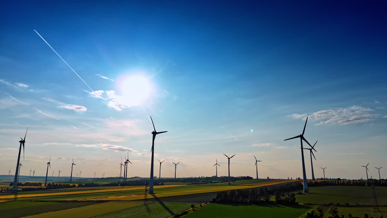 Beautiful agricultural plantations with wind turbines rotating in the wind. Low angle view at the green energy producers at the backdrop of blue sky.