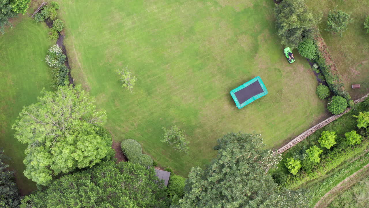 Static Aerial Shot of Man Mowing Lawn on Summer’s Day using Ride On Lawnmower from Birds Eye View Perspective
