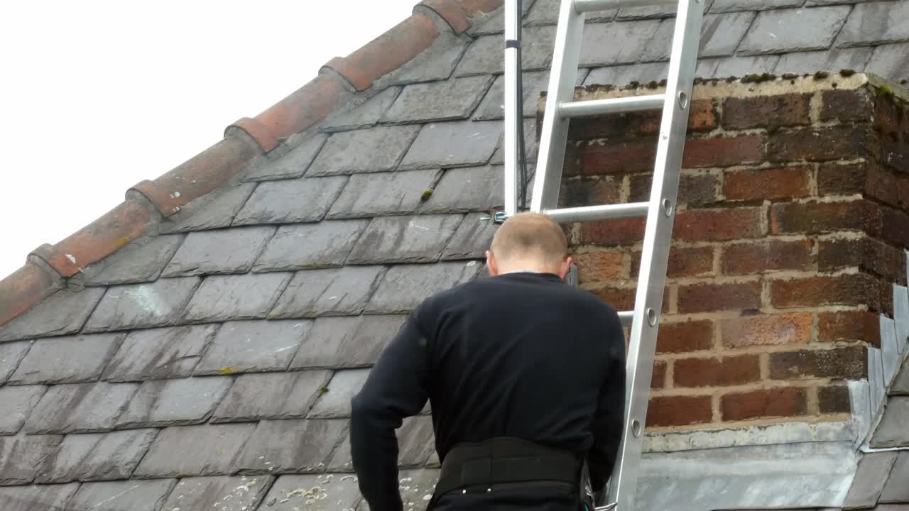 Man on ladder installing digital television aerial on home chimney