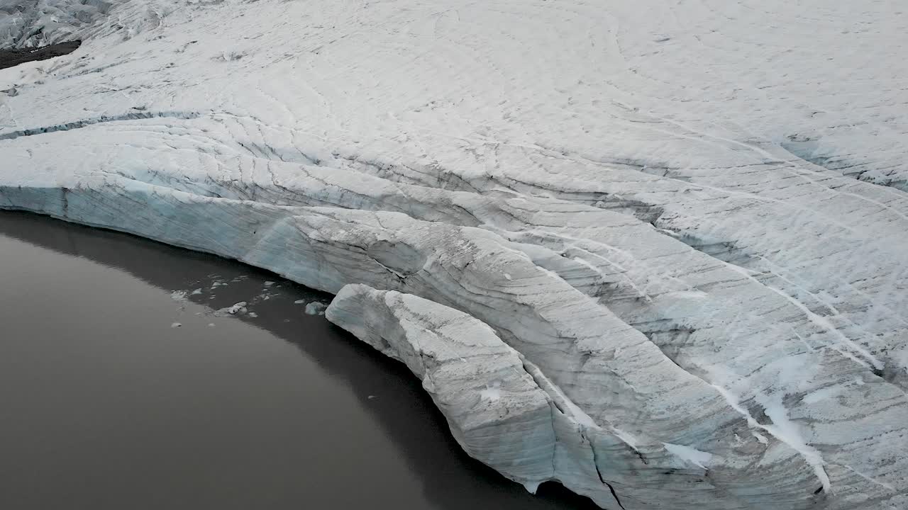 Aerial flyover over the glacial lake and ice of the Claridenfirn glacier in Uri, Swizerland with large crevasses at the water's edge