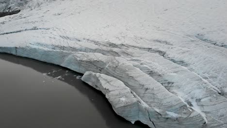 Aerial flyover over the glacial lake and ice of the Claridenfirn glacier in Uri, Swizerland with large crevasses at the water&#039;s edge