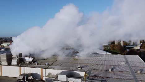 wide shot thick industrial smoke bellows from chimney above warehouse