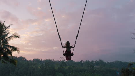 tourist woman swinging over tropical jungle at sunrise travel girl enjoying exotic vacation sitting on swing in having fun holiday lifestyle freedom 4k