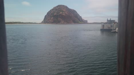 Gimbal-close-up-shot-pushing-through-framed-wood-posts-towards-Morro-Rock-in-the-marina-at-Morro-Bay,-California