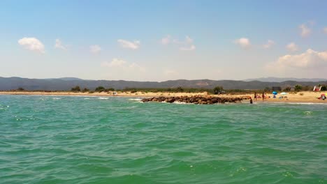 POV-from-a-moving-boat-sailing-through-the-ocean-water-looking-at-a-small-empty-tropical-beach