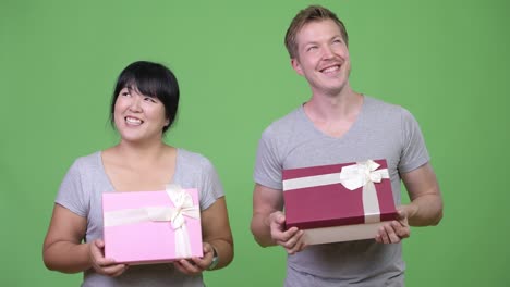 young happy multi-ethnic couple holding gift box and thinking together