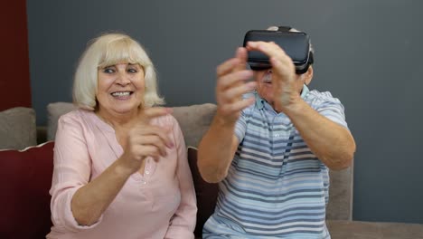 Senior-man-playing-game-in-virtual-reality-headset-glasses,-woman-laughing-with-him-action-at-home