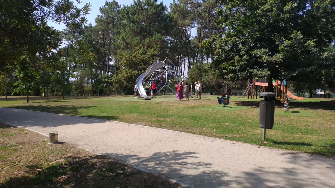 familias con niños jugando en el tobogán del parque público con sus jardines y árboles en una soleada mañana de verano