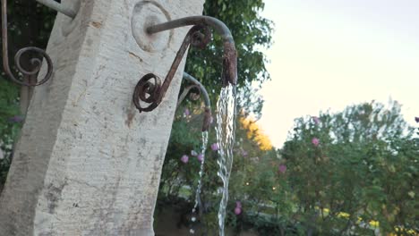 Slow-motion-footage-of-water-flowing-from-a-rusty-spout-on-an-outdoor-fountain