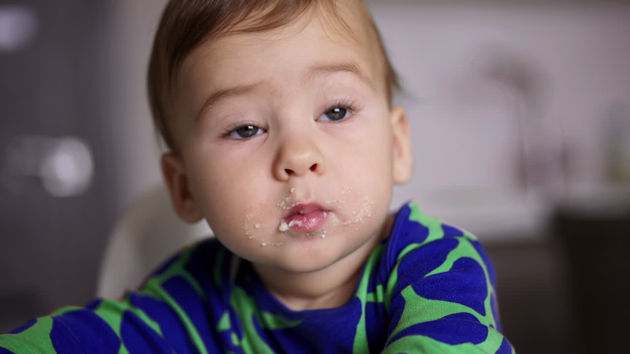 Grey-eyed lovely baby with smudged face. Close up. Little kid eating dairy. Child nutrition. Blurred backdrop.