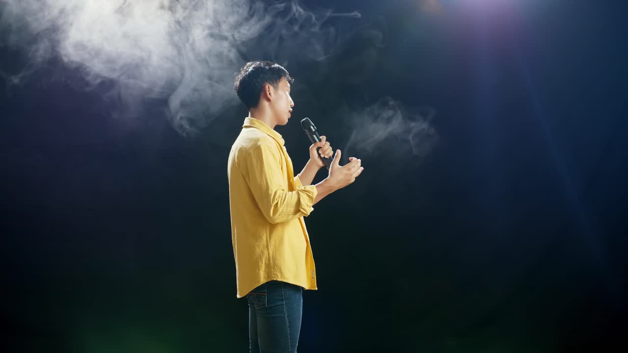 젊은 아시아 소년이 마이크를 들고  연기 검은 배경에서 노래하는 측면 시각