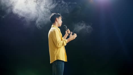 vista lateral de un joven asiático con un micrófono y cantando sobre el fondo blanco de humo negro