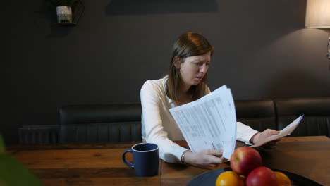 A-stressed-young-brunette-woman-looking-at-a-letter-paperwork-and-bills-on-the-table-as-she-is-worried-and-depressed-in-the-kitchen-at-home