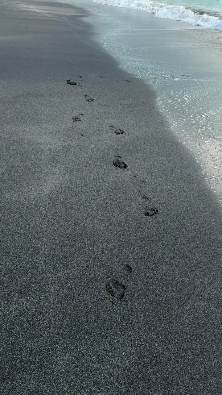 Impronte sulla Spiaggia di Sabbia Scura con Dolci Onde dell'Oceano