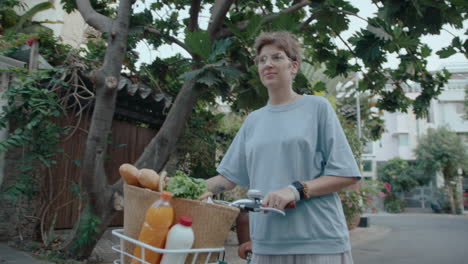 girl walking with bike along the street and carrying groceries on it